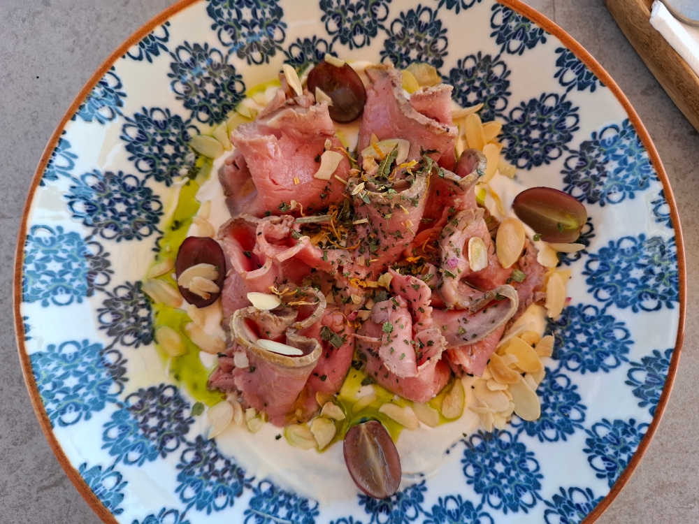 Roastbeef Carpaccio vom zarten Ochsen, mit Kichererbsencreme, Nüssen und Trauben.